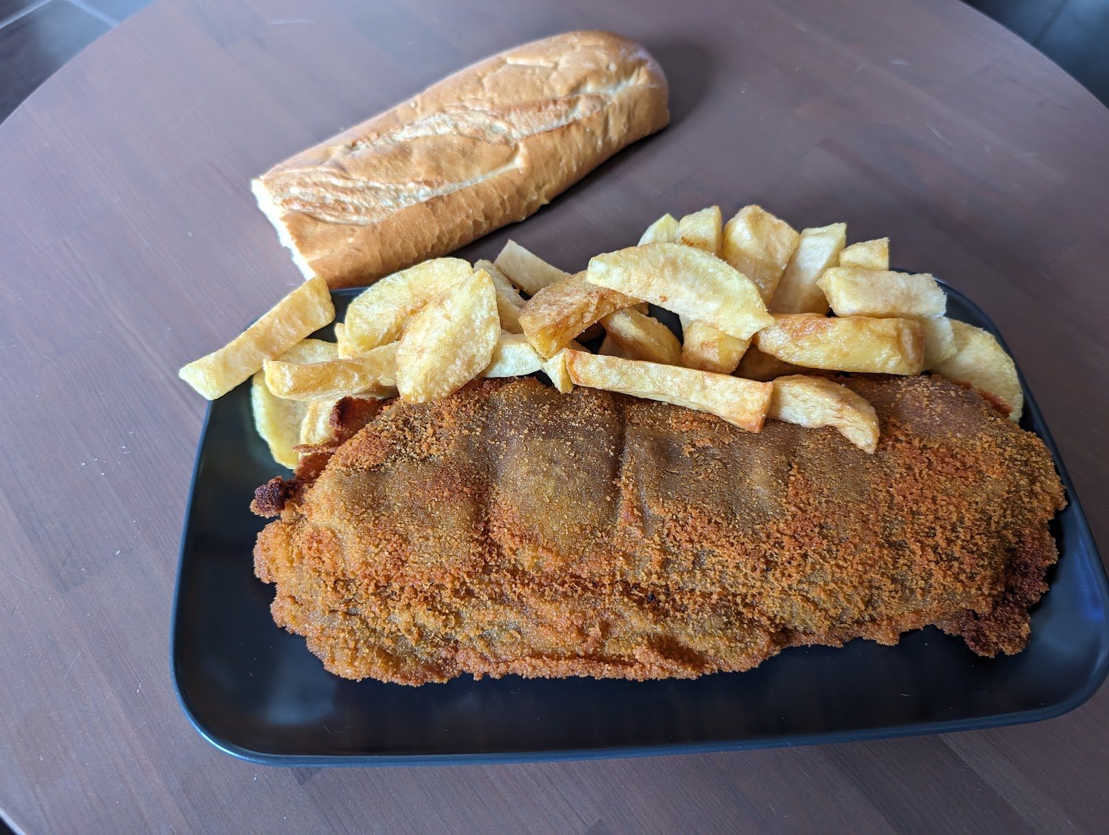 Filete empanado de ternera con patatas fritas caseras, servido en plato de bar.