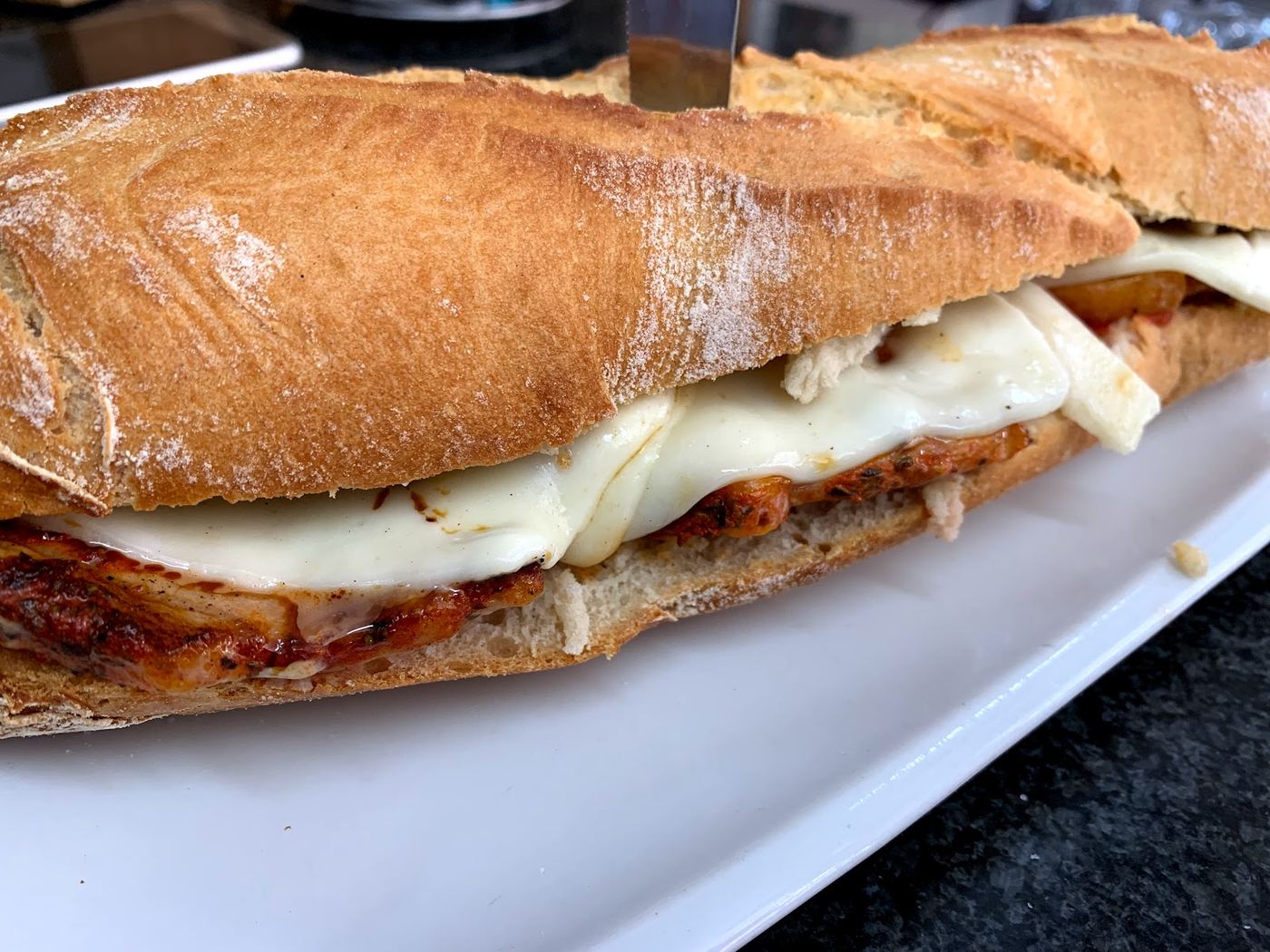 Bocadillo caliente de pollo con queso fundido y salsa especial, cortado por la mitad.